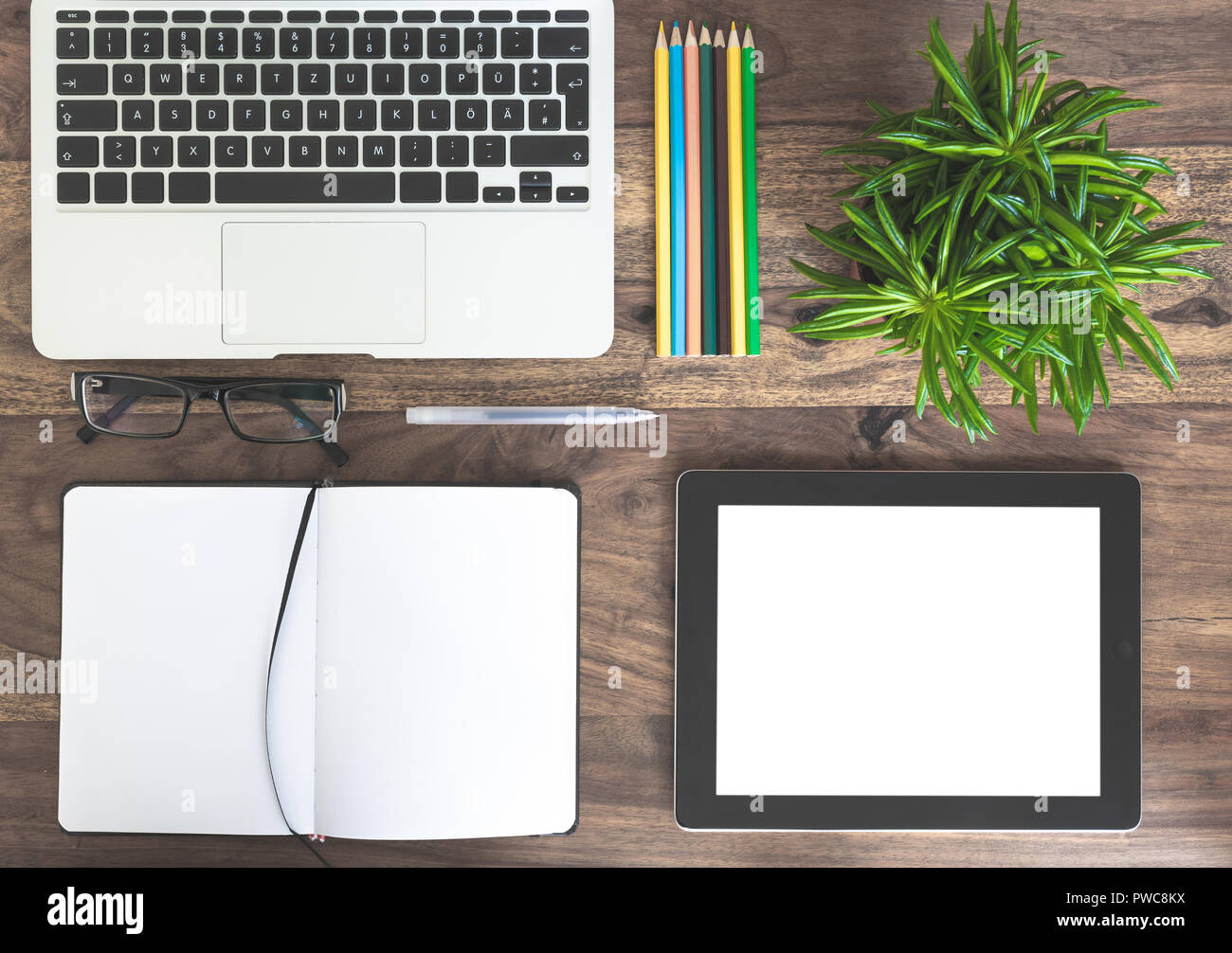 Blocco note, laptop, pianta verde e tablet PC sulla scrivania in legno Foto Stock