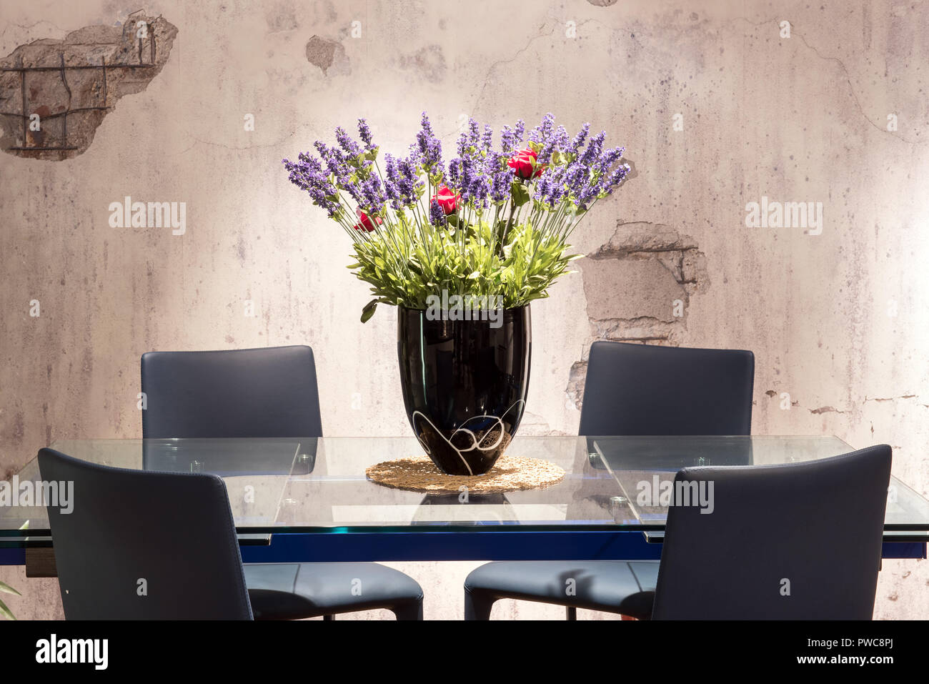 Tavolo da pranzo con centrotavola floreali con colorati di blu e di rosso dei fiori in un vaso e una texture di sfondo grigio parete Foto Stock