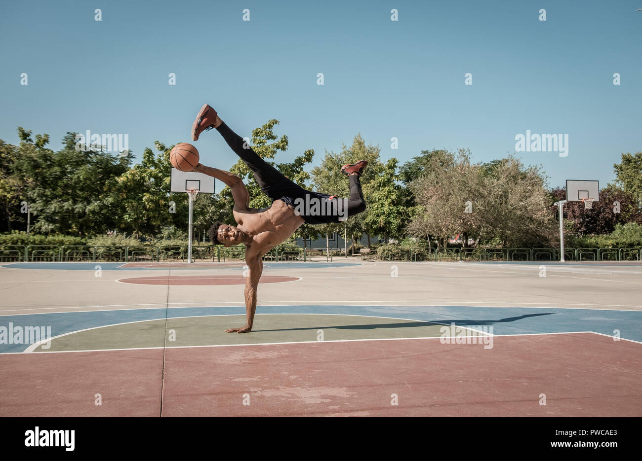 Uno afroamerican giovane senza tshirt sta facendo in equilibrio con una palla da basket in un parco a Madrid durante l'estate a mezzogiorno. Foto Stock