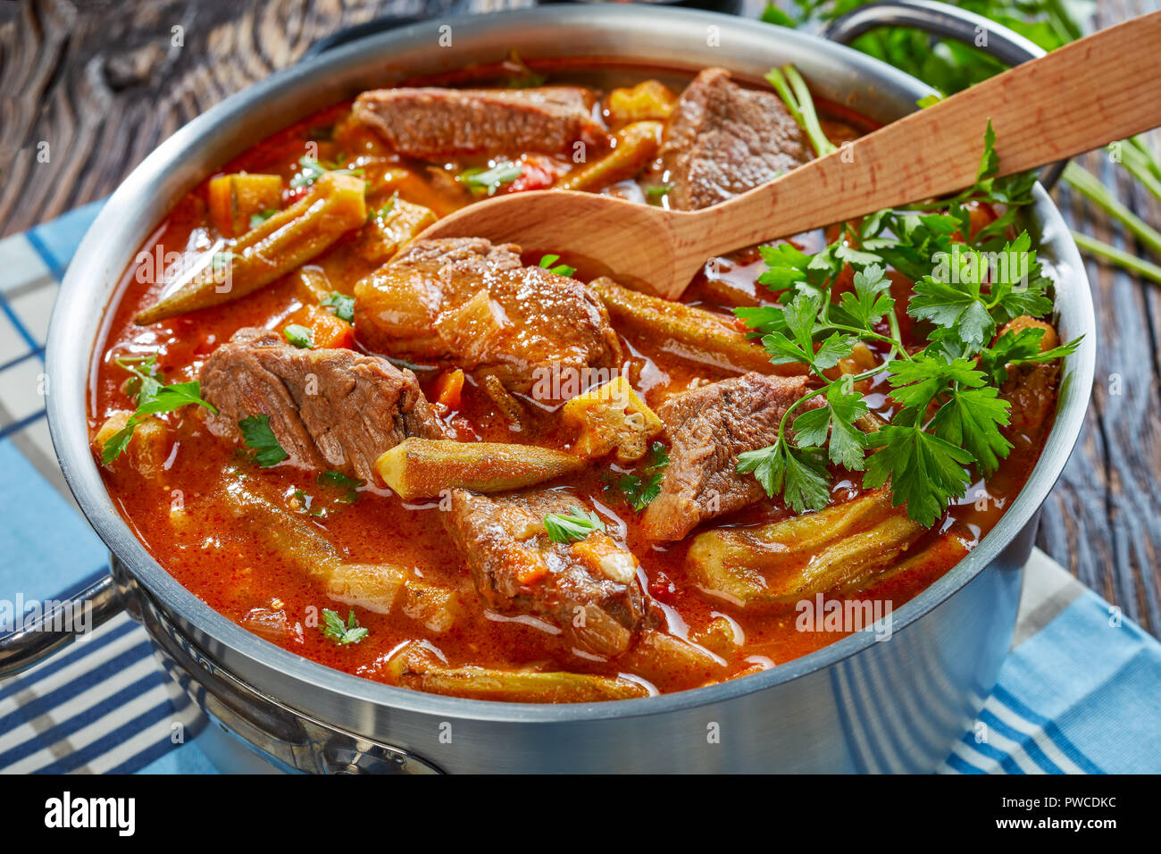 Deliziosa carne di manzo e Okra stufare in una casseruola di metallo con cucchiaio, su un vecchio tavolo di legno, vista da sopra, close-up Foto Stock