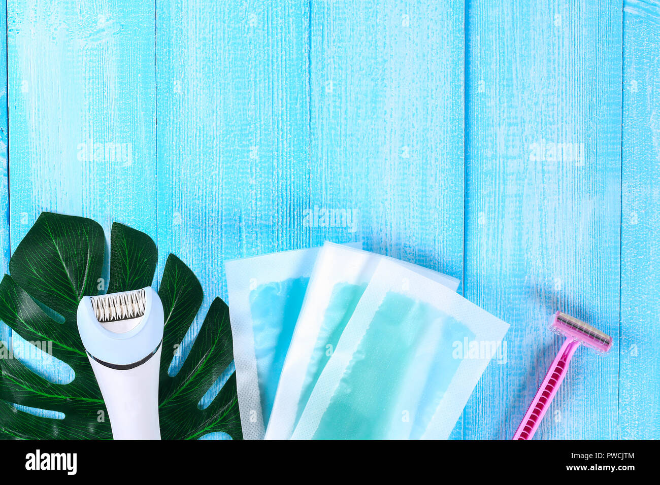 Mezzi per la rimozione dei peli. Epilatore, rasoio per rasatura, strisce di cera su una foglia tropicale su un blu sullo sfondo di legno. Epilazione, depilazione, rasatura Foto Stock