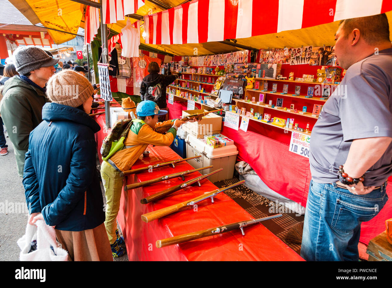 Bambini giapponesi della galleria di tiro in stallo durante il festival. Ragazzo apprendimento in azienda contatore fucile in entrambe le mani tenendo mira a un bersaglio. Foto Stock