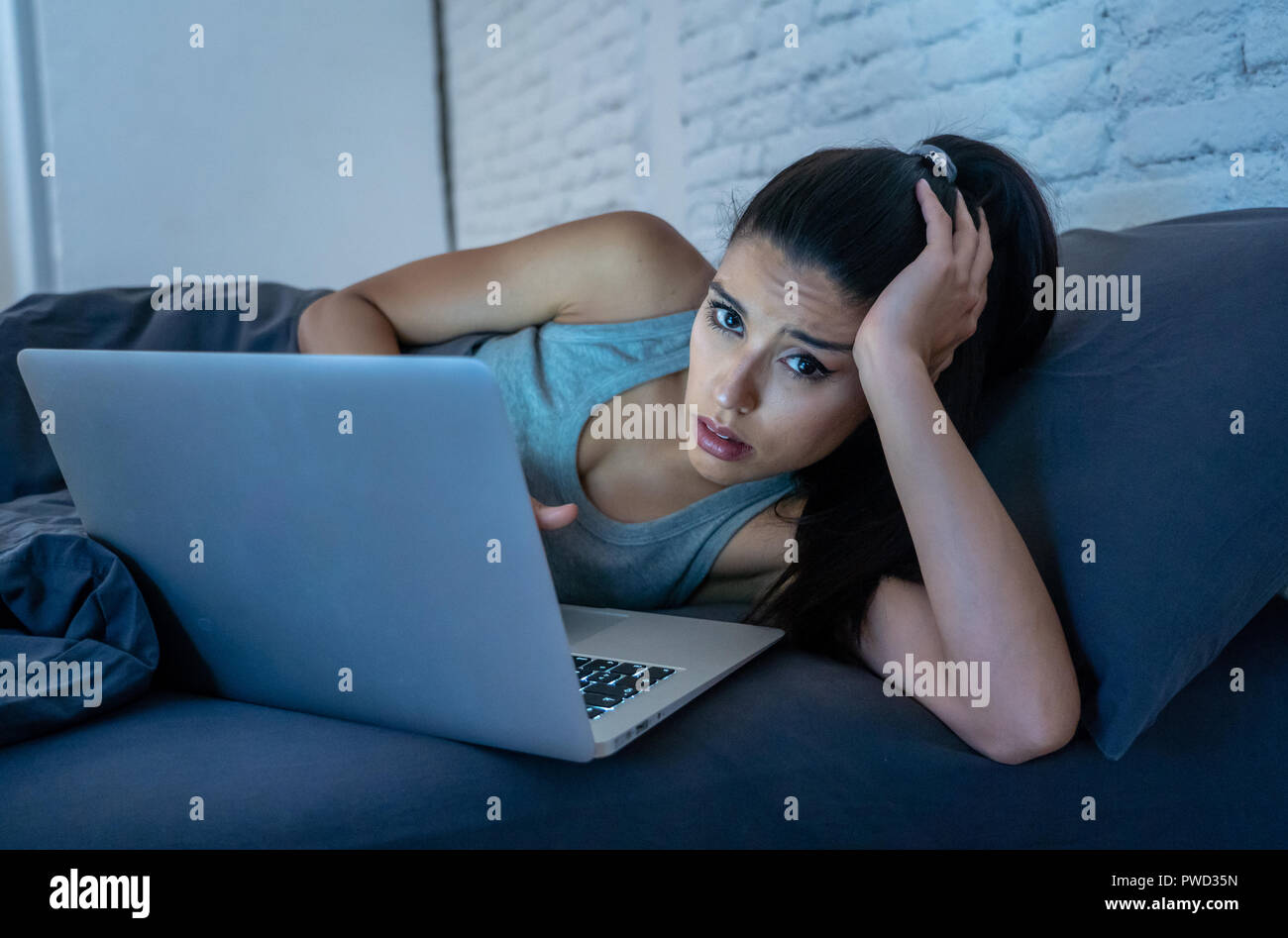 Stanco attraente giovane donna che lavorano e navigare su internet con il computer sul divano di casa a tarda notte in dipendenza da internet e superlavoro co Foto Stock