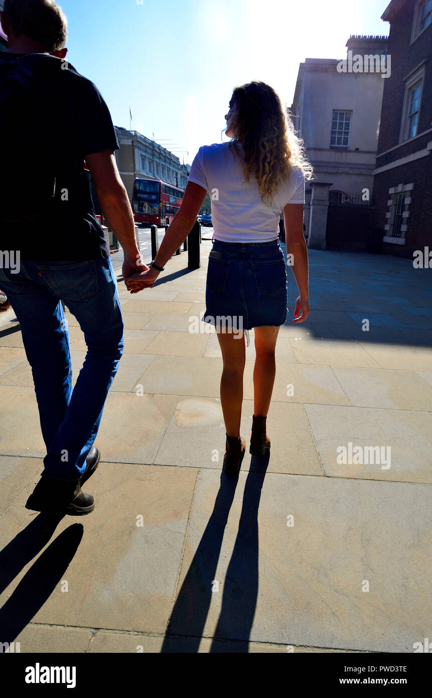 Coppia giovane camminando mano nella mano in Whitehall, Londra, Inghilterra, Regno Unito. Retroilluminati Foto Stock