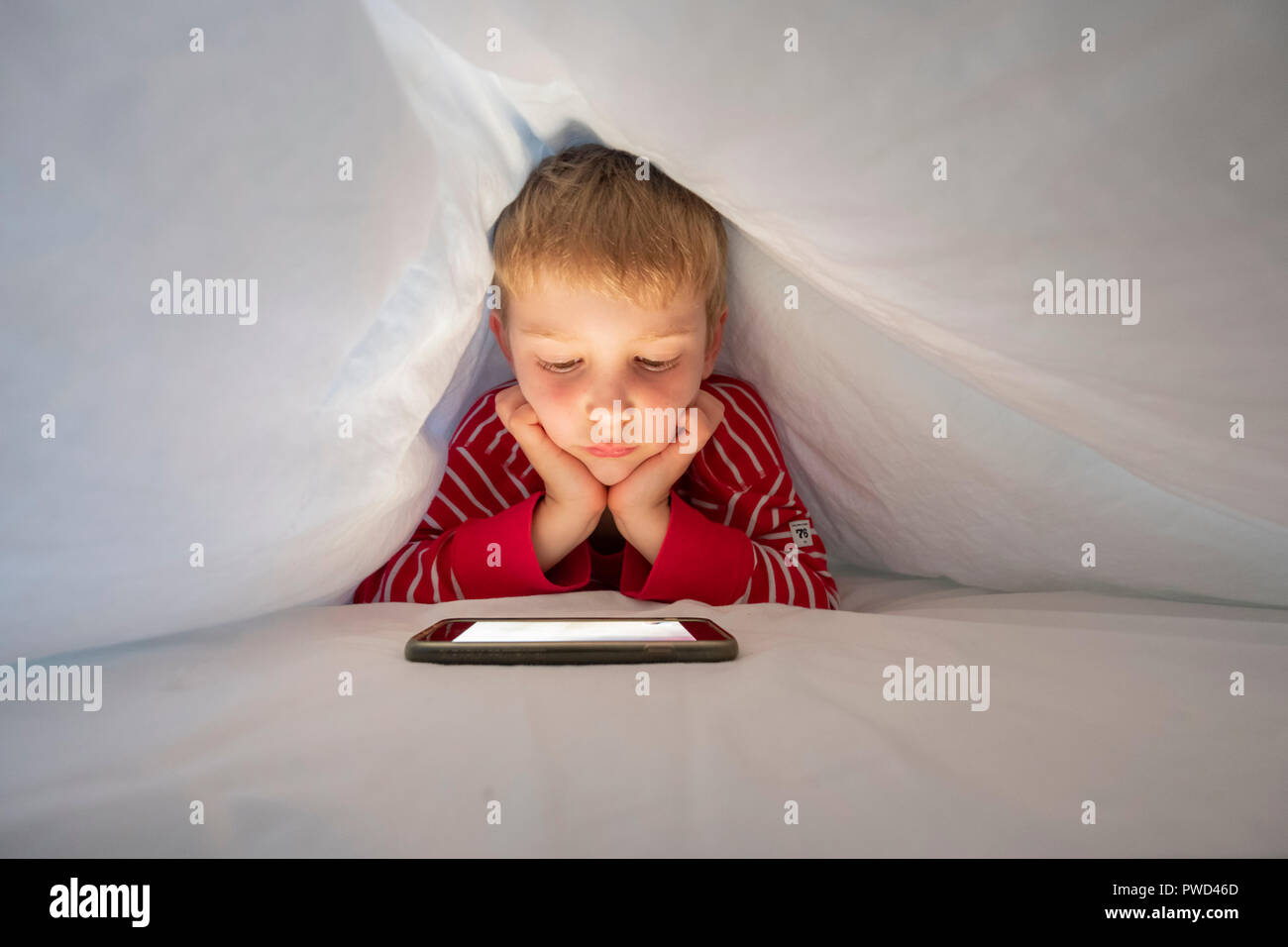 Ragazzo caucasica nel suo letto utilizza lo smartphone per effettuare la chiamata video per parlare a un amico Foto Stock