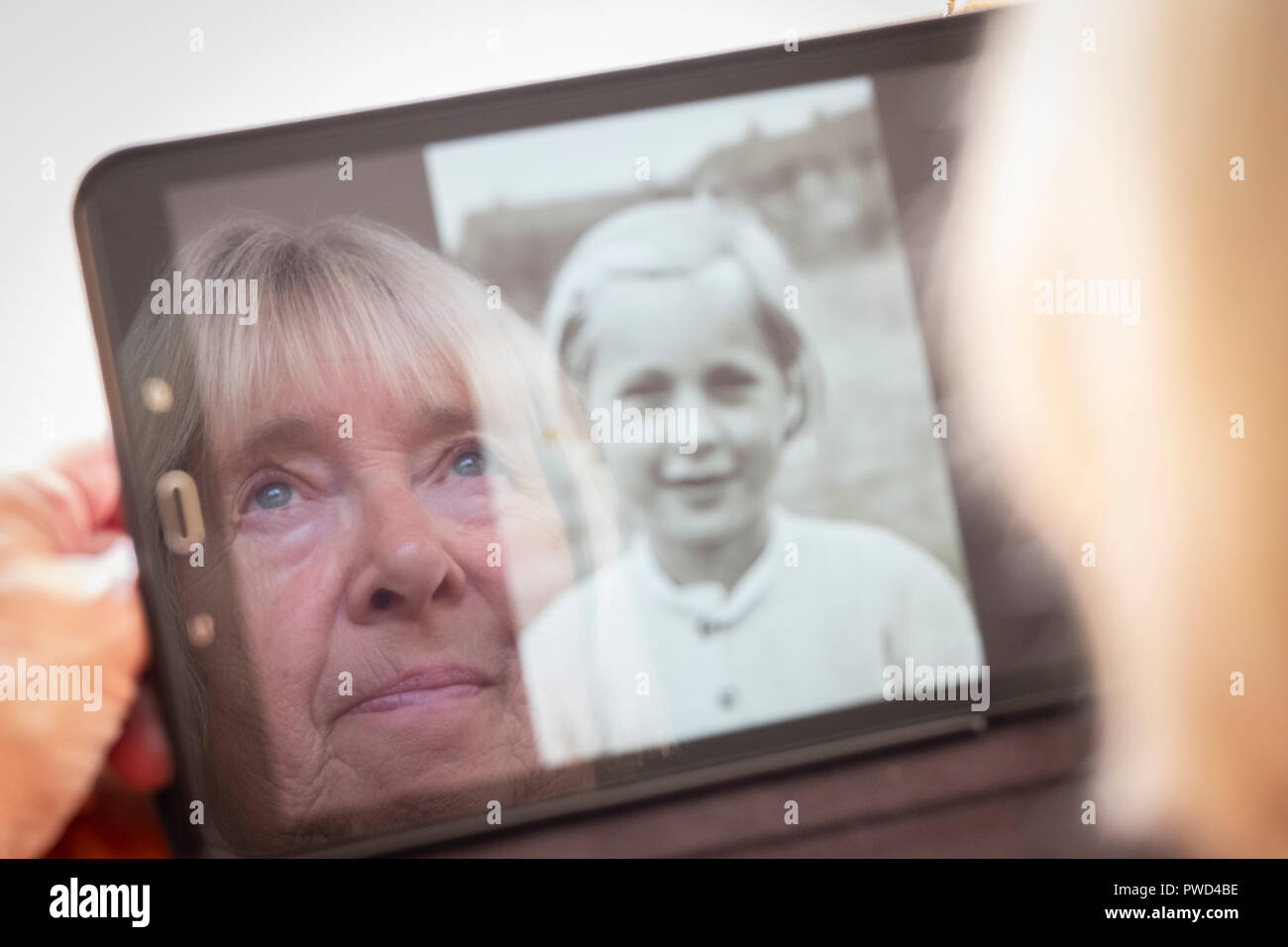 Senior donna caucasica guardando le vecchie foto di se stessa come una giovane donna in un computer tablet Foto Stock