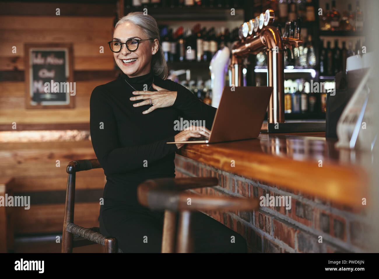 Senior bella donna seduta al cafe contatore con laptop che guarda lontano e sorridente. Allegro coppia donna d'affari presso la caffetteria con il computer portatile. Foto Stock