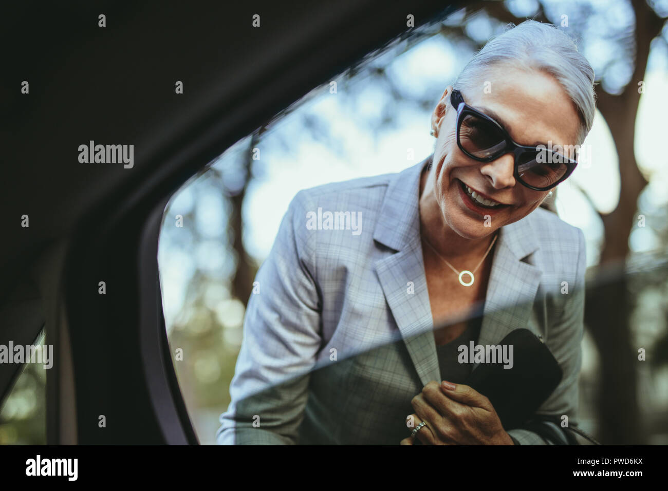 Felice senior donna che guarda all'interno dell'auto e a parlare con il conducente. Femmina nel business suit parlando con cabina conducente. Foto Stock