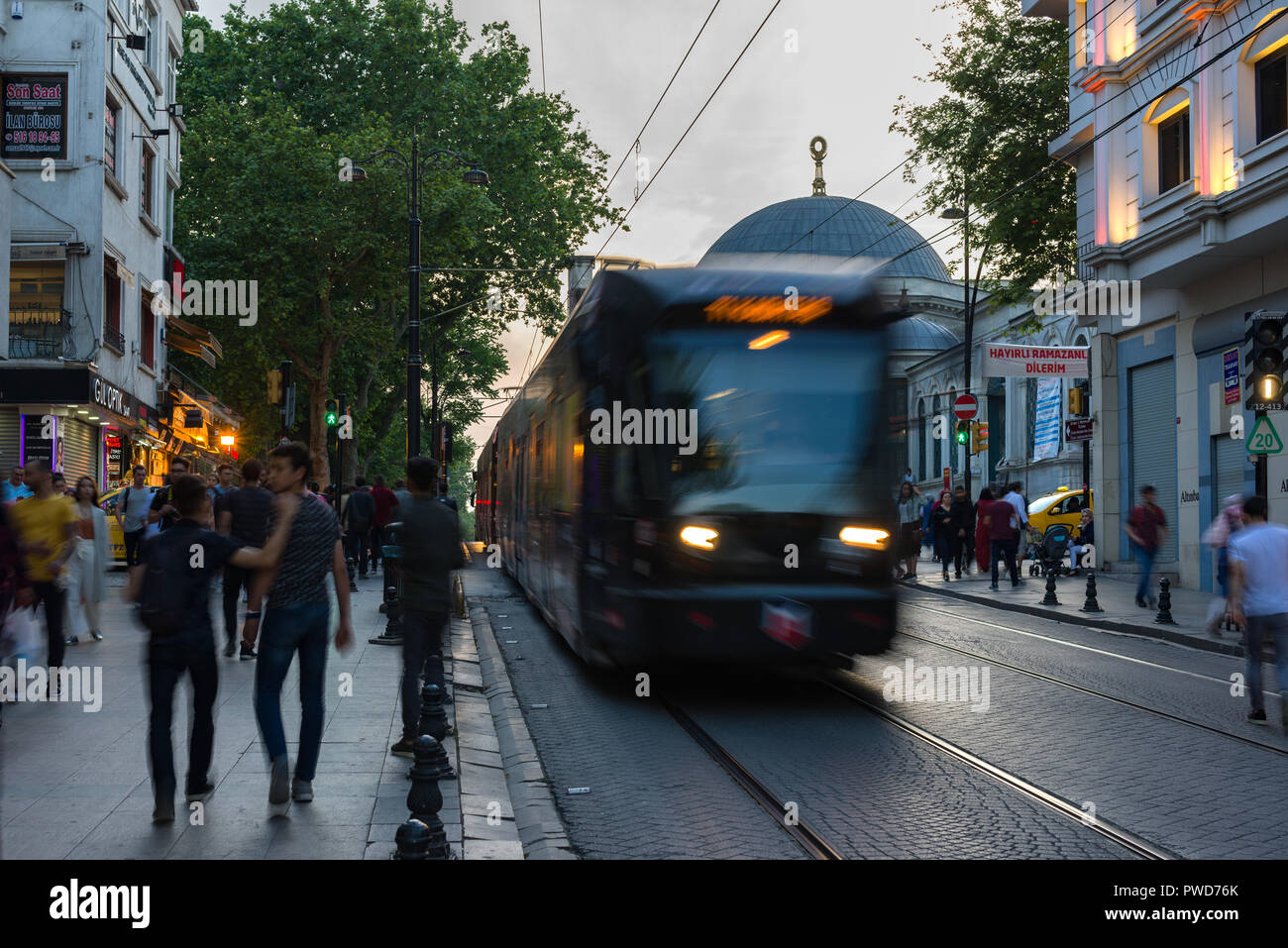 Un rosso T1 Il tram passa lungo una strada come la gente a piedi passato al crepuscolo, Istanbul, Turchia Foto Stock
