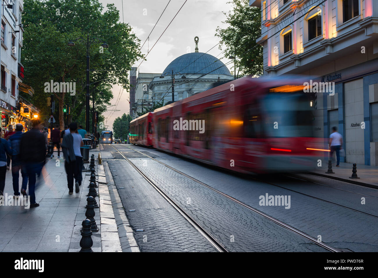Un rosso T1 Il tram passa lungo una strada come la gente a piedi passato al crepuscolo, Istanbul, Turchia Foto Stock