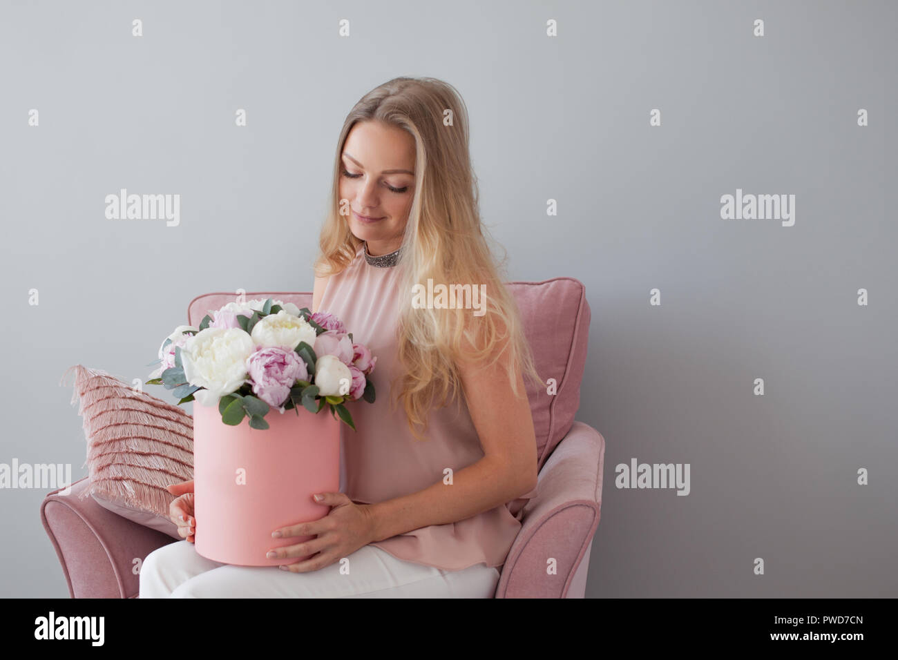 Felice donna bionda con fiori in un cappello box. Bouquet di peonie. Ragazza in un morbido abito rosa con una rosa bouquet di peonie Foto Stock