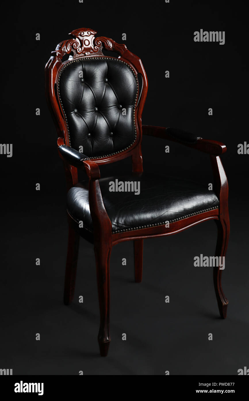 Vecchio nero sedia rivestita in cuoio su sfondo nero. Foto Stock