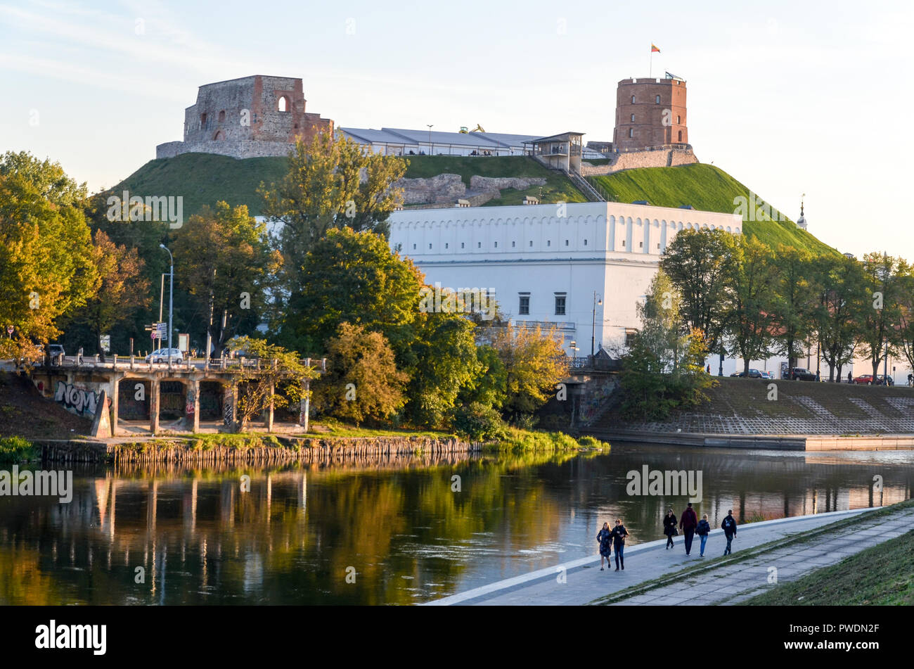 Gediminas Hill e il castello di torre, a Vilnius, Lituania, dal fiume Neris, con la gente che camminava sul lungomare Foto Stock