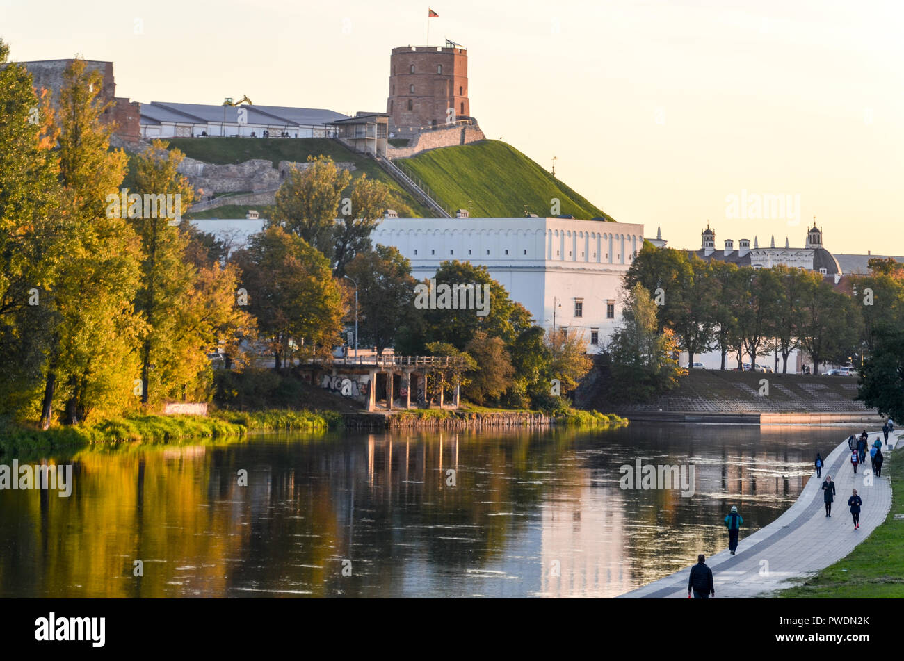Gediminas Hill e il castello di torre, a Vilnius, Lituania, dal fiume Neris, con la gente che camminava sul lungomare Foto Stock