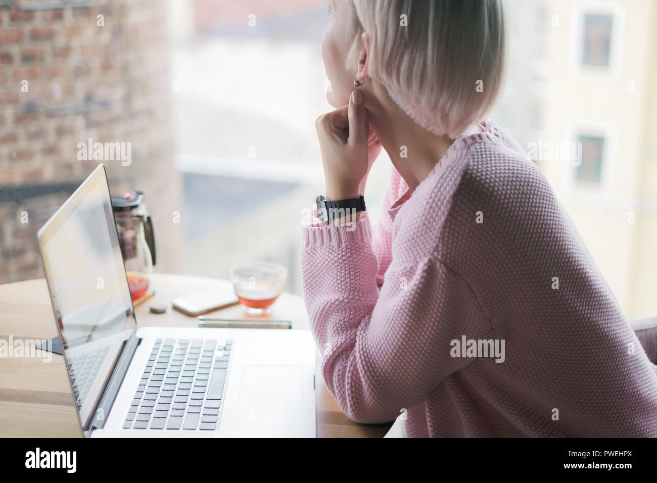 Bella donna caucasica sognare qualcosa mentre è seduto con il computer portatile in un cafe bar che guarda lontano in corrispondenza della finestra. Lei sta pensando di nuovo id Foto Stock