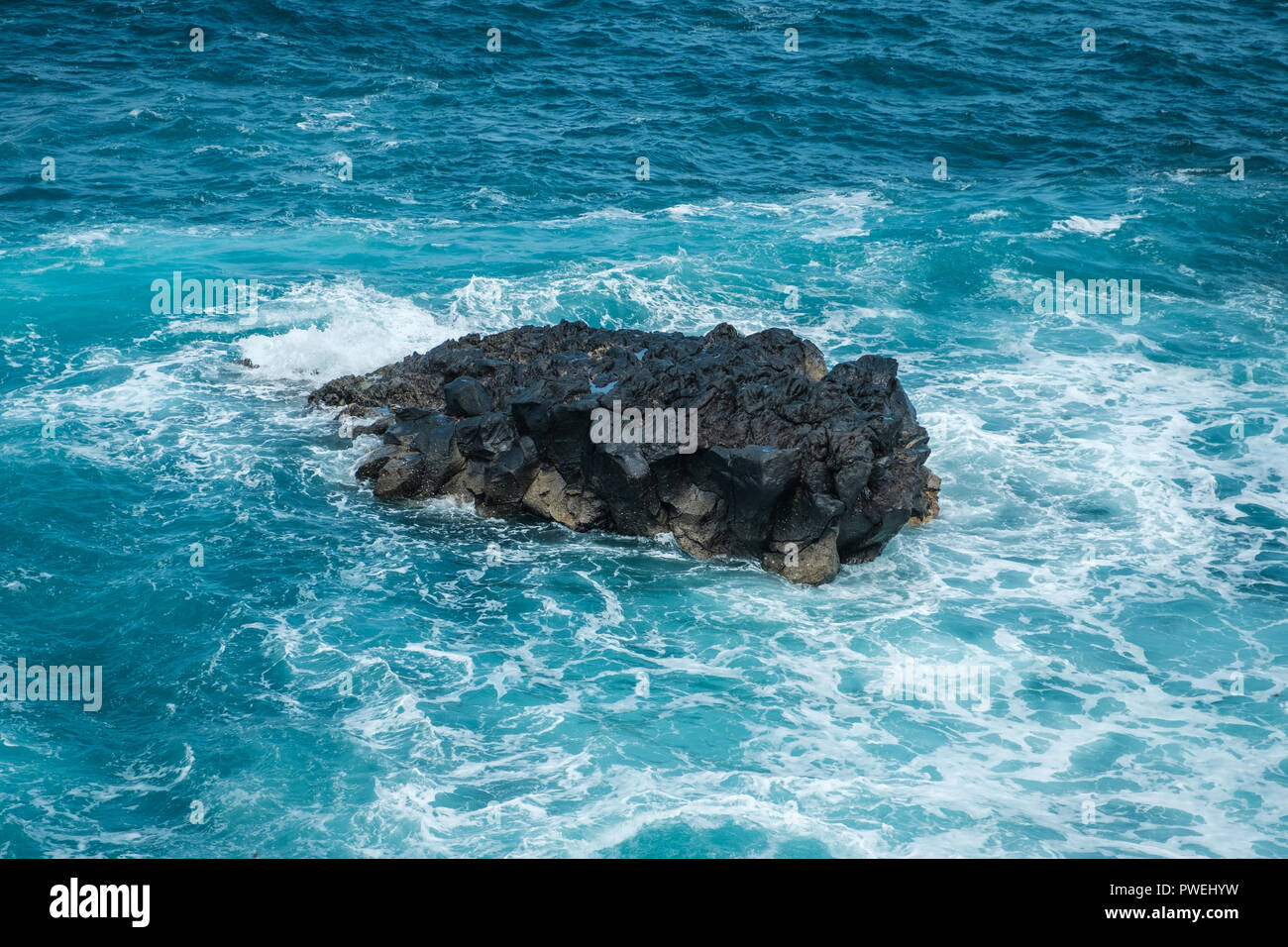 Onde che si infrangono contro le rocce nere in ocean Foto Stock