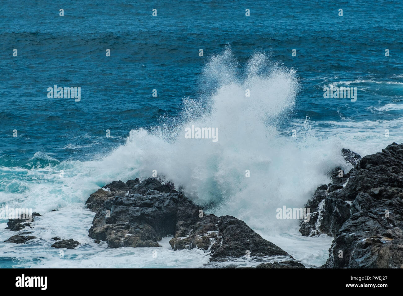 Oceano onde che si schiantano contro rocce nere sulla costa - Foto Stock