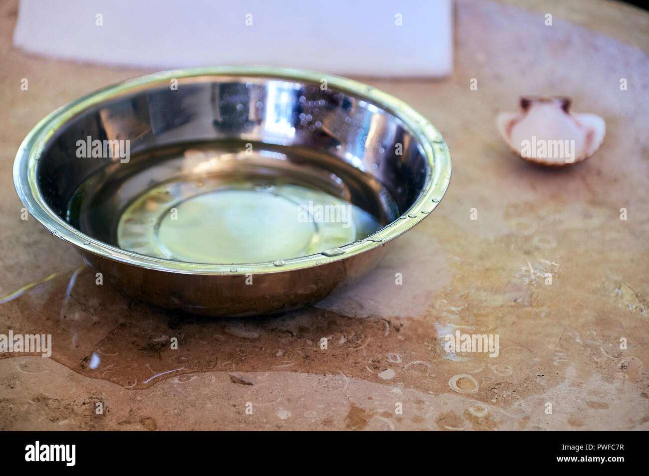 Dettaglio della vasca battesimale in marmo in chiesa. Un vaso di acciaio, una conchiglia di mare Foto Stock Dettaglio della vasca battesimale in marmo in chiesa. Un vaso di acciaio, una conchiglia di mare Foto Stock