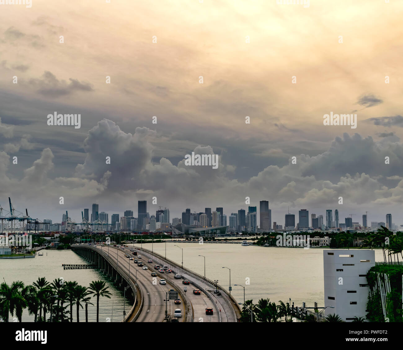 Dark nuvole temporalesche telaio sopra il centro cittadino di Miami al tramonto come un costante flusso di traffico attraversa il MacArthur Causeway a Miami Beach Foto Stock