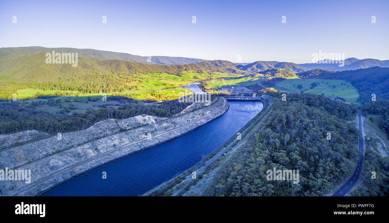 Panoramica aerea di canale d'acqua portando a Tumut Power Station e bellissime colline al tramonto. NSW, Australia Foto Stock