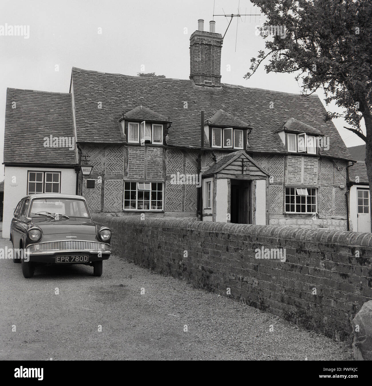 Anni sessanta, Hardwick, Aylesbury, Bucks, una Ford Anglia station wagon parcheggiata fuori in un vialetto accanto a un legno storico-incorniciato casa in home counties, Inghilterra, Regno Unito. Foto Stock