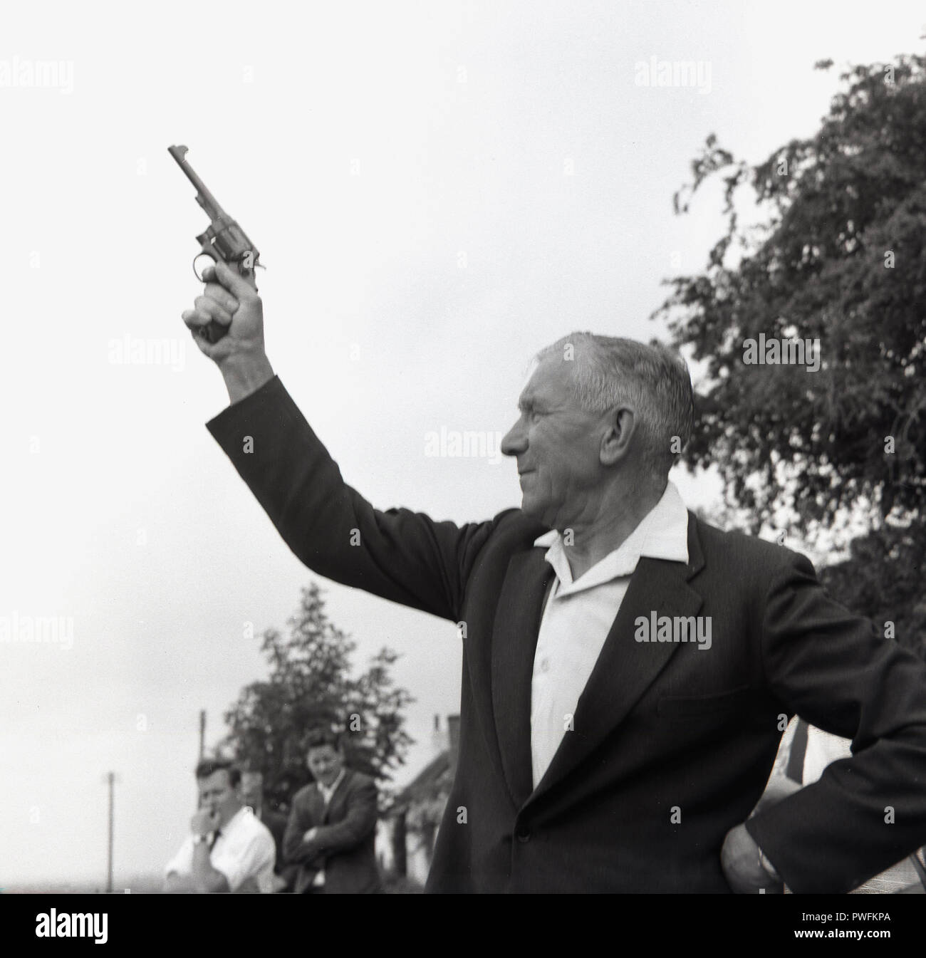1967 l'uomo utilizzando una pistola di avviamento del motorino di avviamento o al di fuori di pistola in un villaggio di fete, di annunciare l'inizio del rimorchiatore della guerra contest, Bucks, Inghilterra, Regno Unito. Un motorino di avviamento per una pistola è una pistola vuota e viene cotta per avviare concorsi sportivi, in particolare la via e il campo gare. Foto Stock
