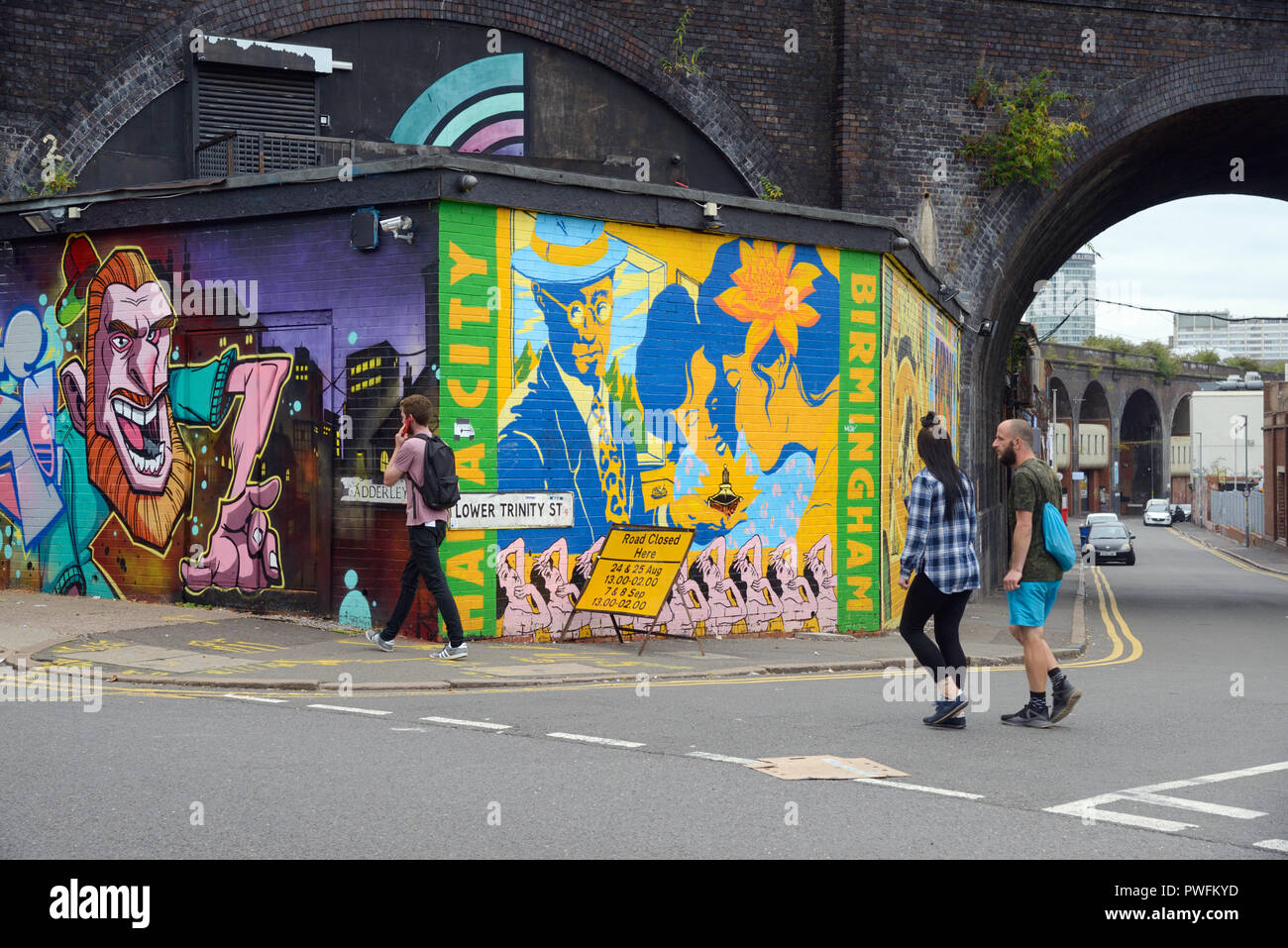 Coppia giovane & Man a piedi passato Arte di Strada nel vecchio Run-Down strade di Digbeth Birmingham Inghilterra Foto Stock