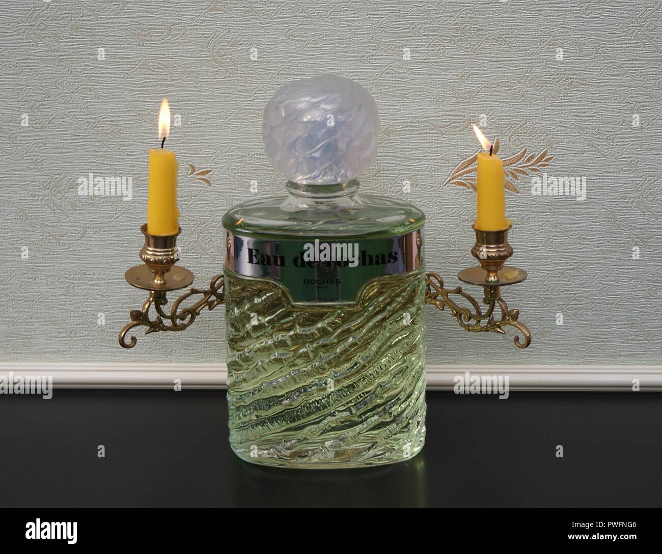 Eau de Rochas, fragranza per signore, grande bottiglia di profumo nella parte anteriore di un pianoforte candelabri con brillanti candele Foto Stock