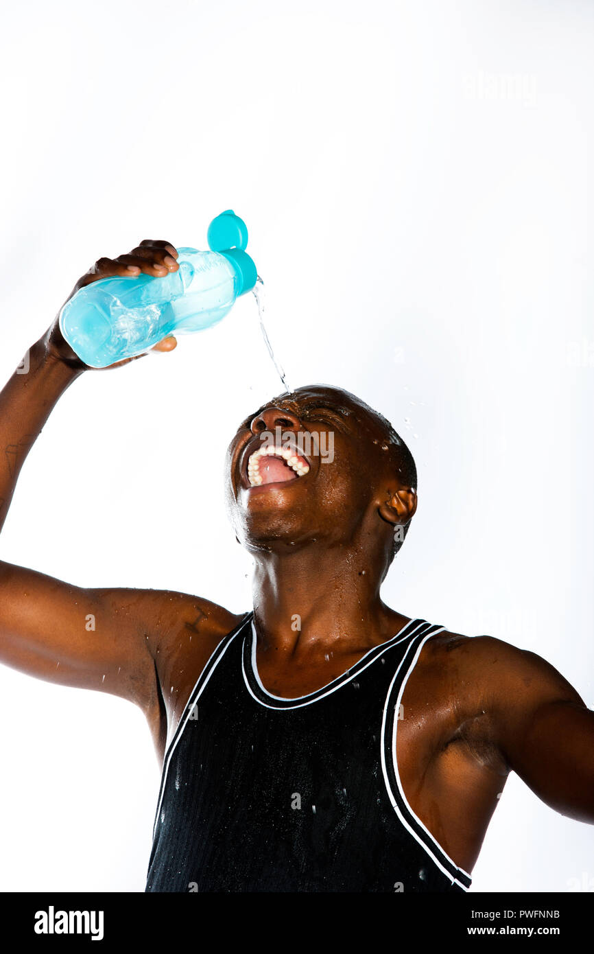 Ridendo african sportive giovane maschio versando acqua fuori di una bottiglia di acqua sulla sua fronte Foto Stock