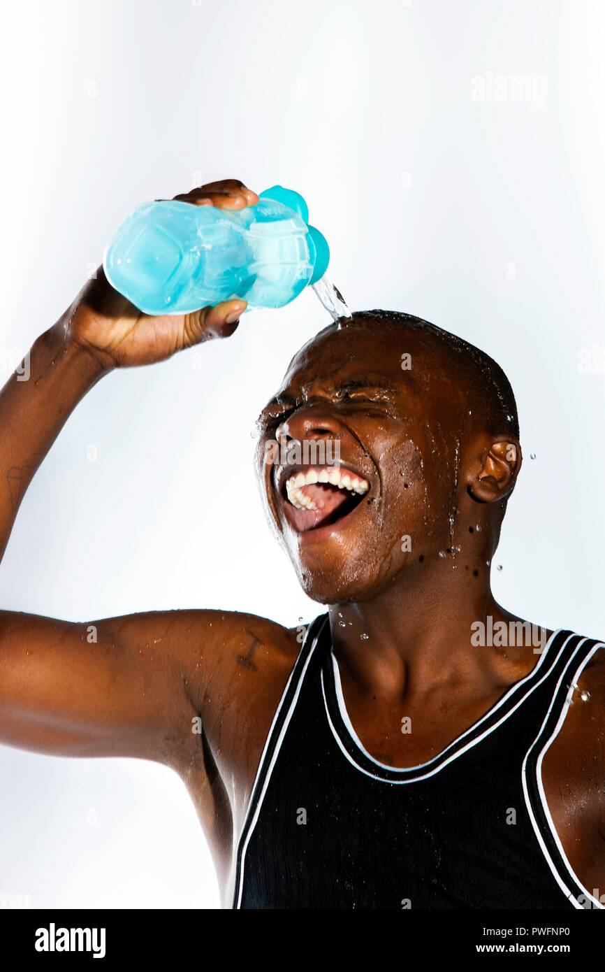 Ridendo african sportive giovane maschio versando acqua fuori di una bottiglia di acqua sopra la sua testa Foto Stock