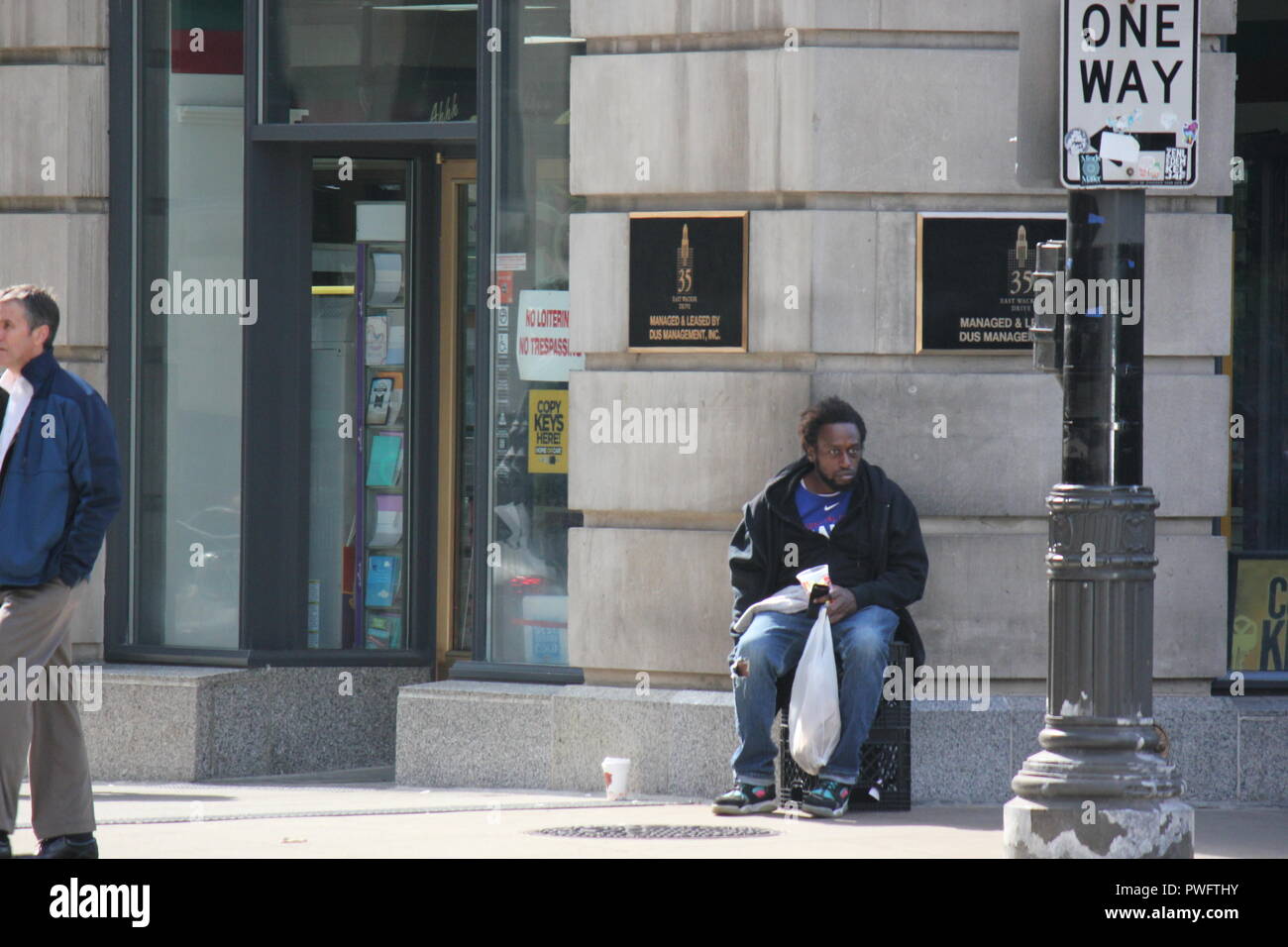 Uno dei molti Chicago's senzatetto seduto su una cassa di latte chinarsi sull'angolo di Wacker Drive e Wabash Avenue, mendicando per una dispensa. Foto Stock
