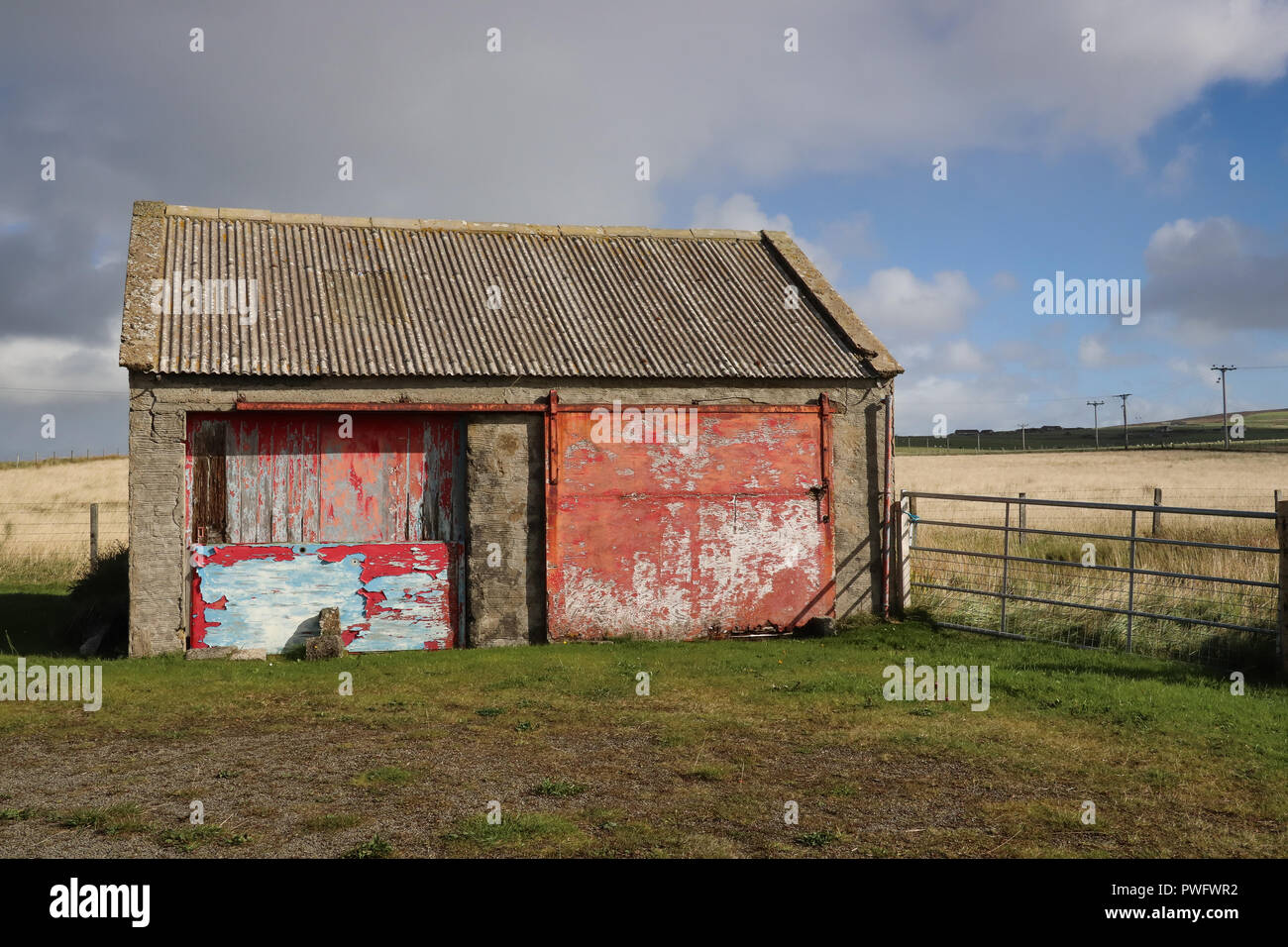 Abbandonati porta due garage nelle Orkney continentale, Scozia, che era stato intavolato con il legno compensato,la sua vivacemente colorato la vernice si stava scrostando off. Campo,bluesky Foto Stock