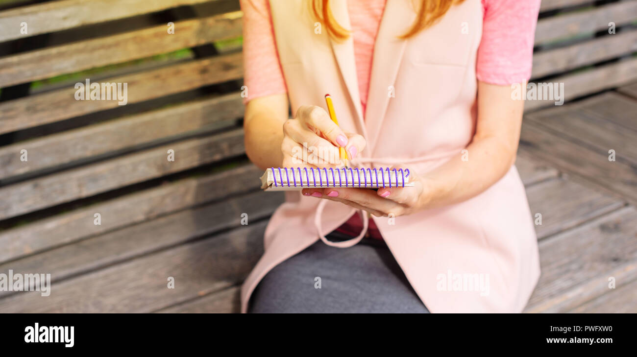 Banner giovane e bella ragazza seduta su una panca in legno nell'aprire la scrittura in un notebook. Giornata di sole lifestyle messa a fuoco selettiva Foto Stock