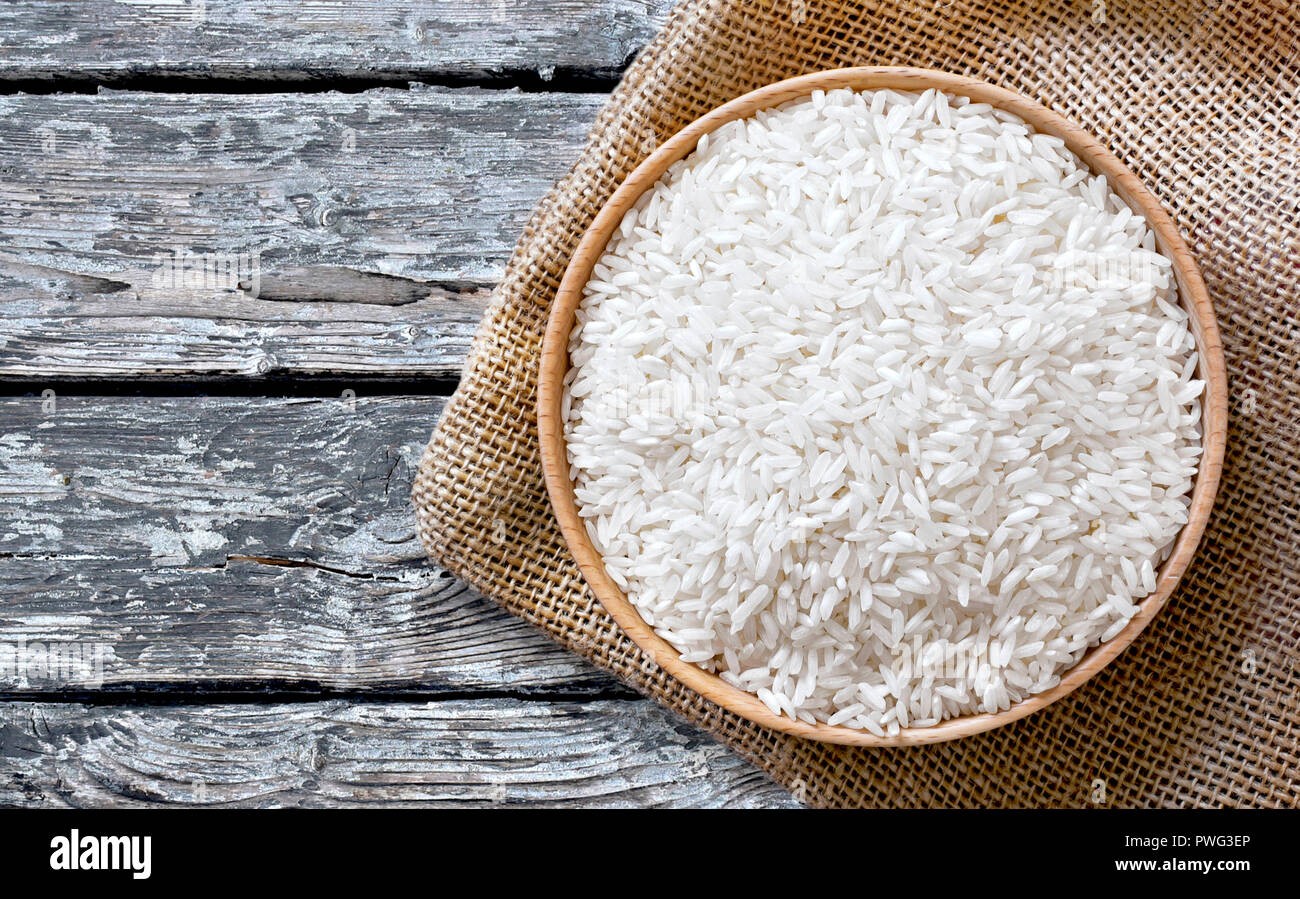 Mangiare sano scena con materie, riso parboiled in una ciotola di legno, vista dall'alto o closeup shot su un weathered tavolo in legno. Foto Stock