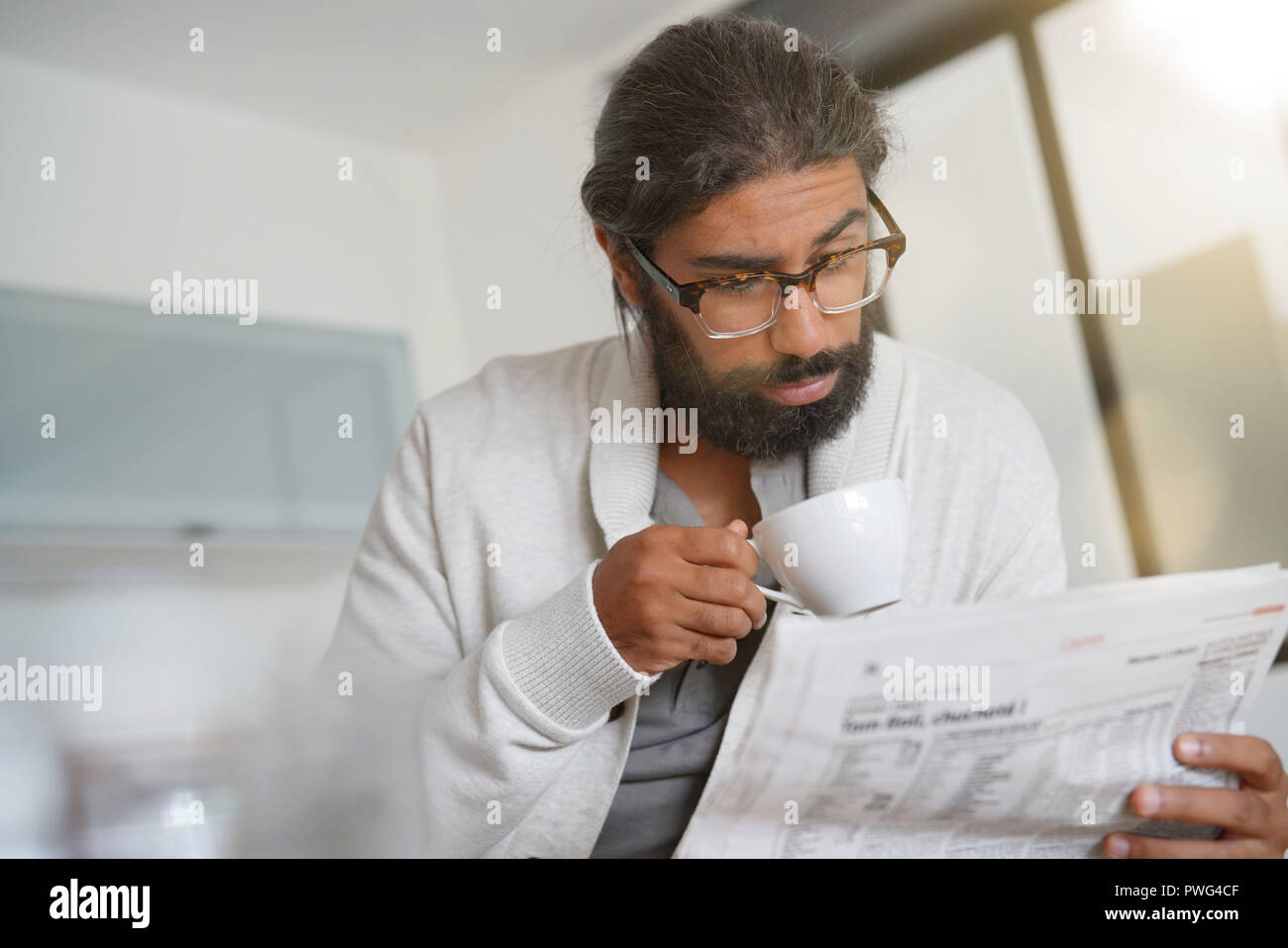 Dai capelli scuri uomo barbuto a casa leggere il giornale Foto Stock