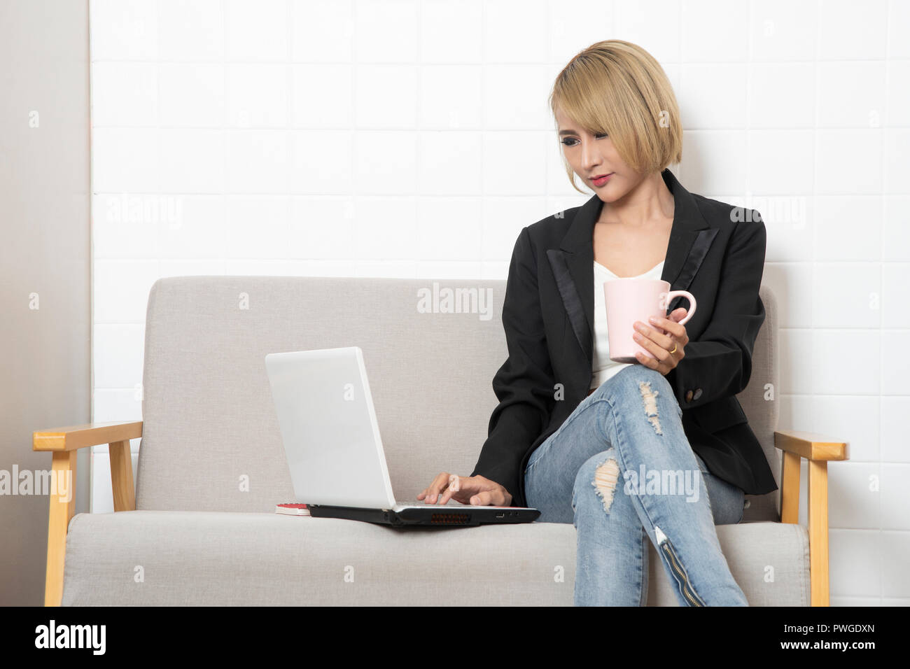 Business donna seduta sul divano e lavorando dal tablet computer tenendo tazza di caffè in mano. Foto Stock