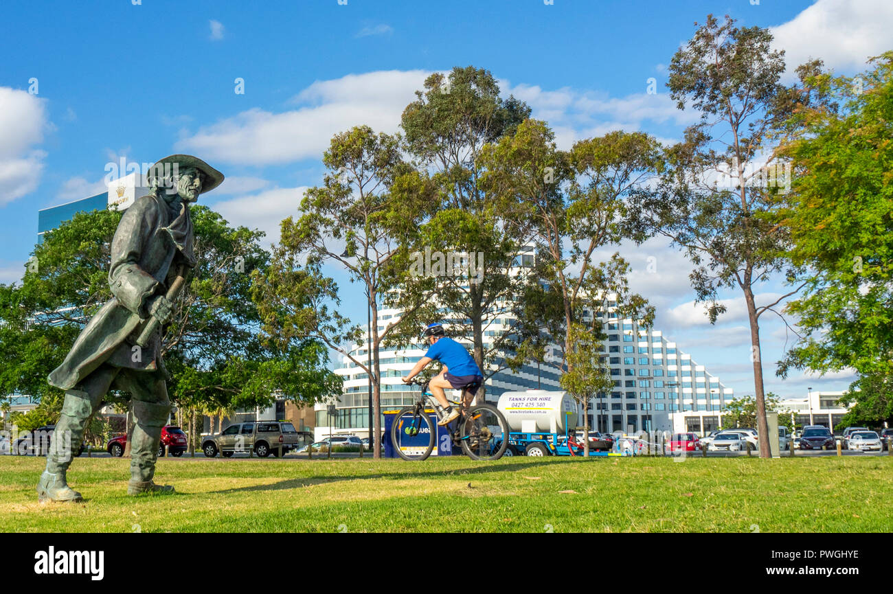 Ciclista in sella ad una bicicletta passato una statua di bronzo di Willem de Vlamingh e Crown Towers e Crown Metropol Hotel di Burswood Perth Western Australia. Foto Stock