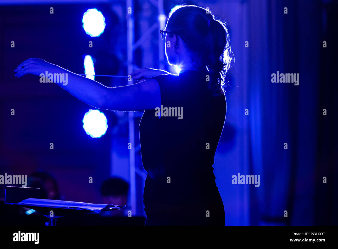 Conduttore femmina dirigere la sua band presso una scuola locale di prestazioni con forte blu luci dello stadio Foto Stock