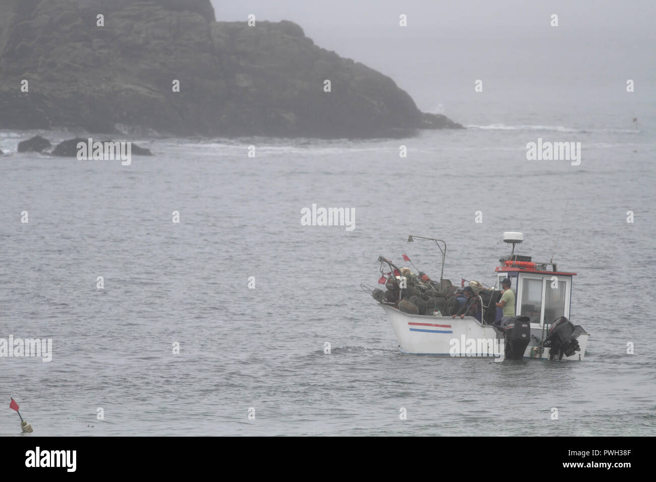 Portoghese tradizionale piccola barca da pesca durante la fatica tra massi. Portoghese settentrionale costa rocciosa in un estate mattinata nebbiosa. Foto Stock