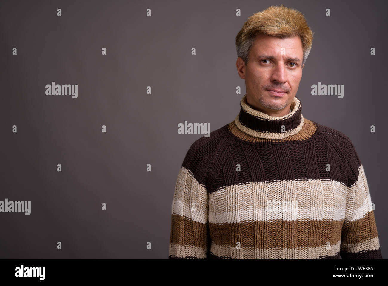 Uomo con capelli biondi che indossa un maglione turtleneck contro il dorso grigio Foto Stock