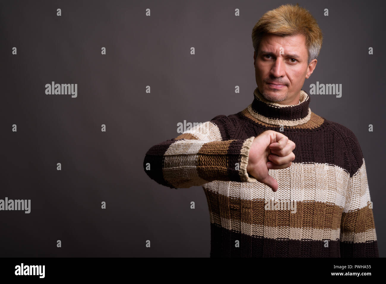 Uomo con capelli biondi che indossa un maglione turtleneck contro il dorso grigio Foto Stock