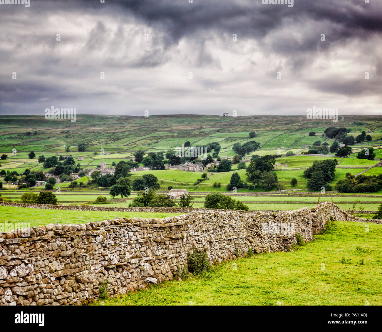 Wensleydale e il villaggio di Askrigg, Yorkshire Dales, Inghilterra, su un giorno nuvoloso con un secco muro di pietra in primo piano. Foto Stock