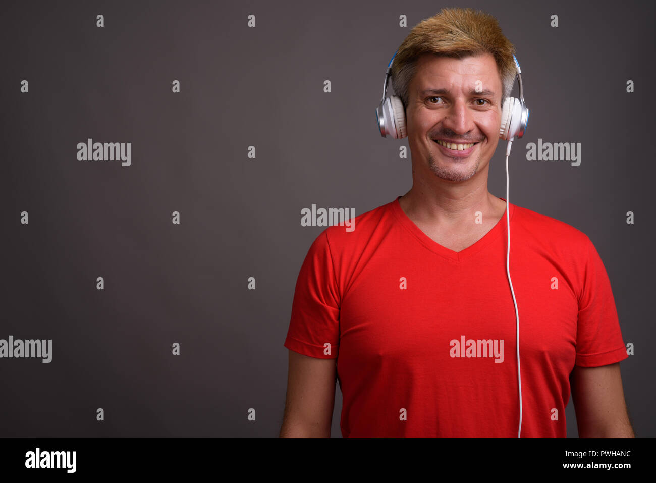 Uomo con capelli biondi ascoltando musica contro lo sfondo grigio Foto Stock