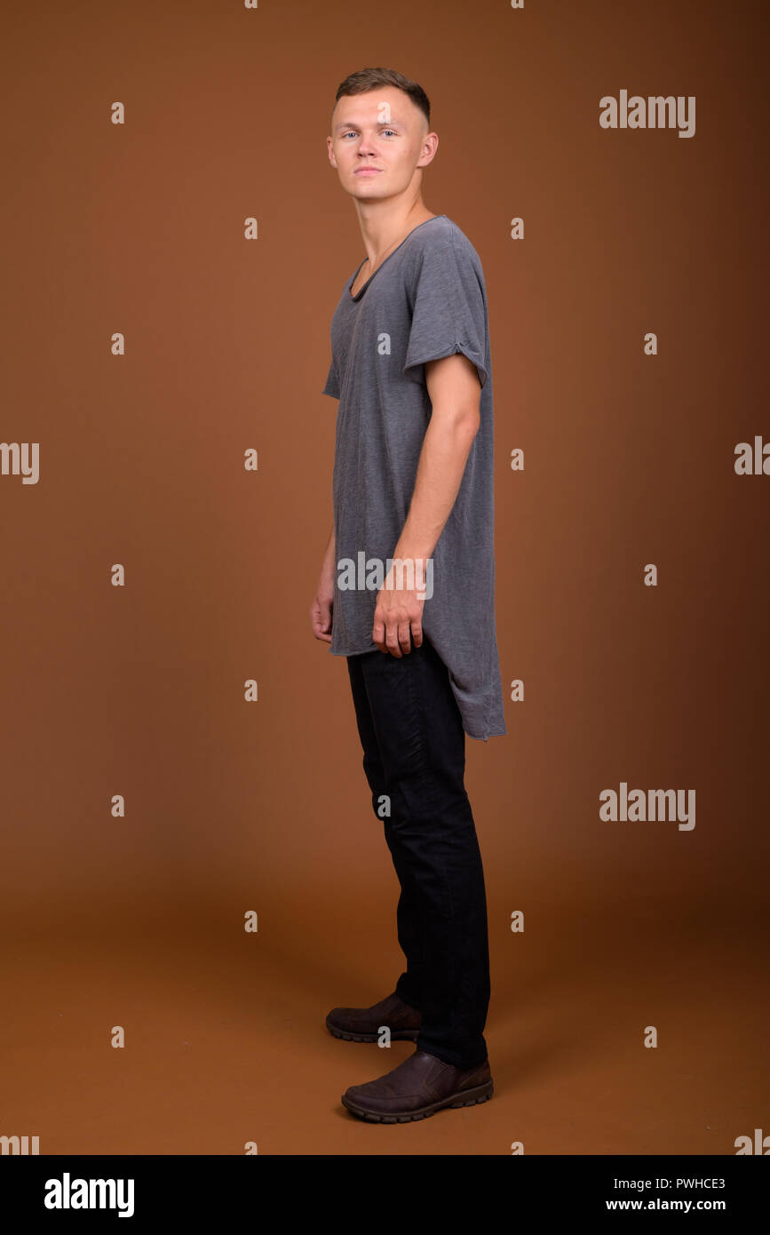 Giovane uomo che indossa maglietta grigio contro sfondo marrone Foto Stock