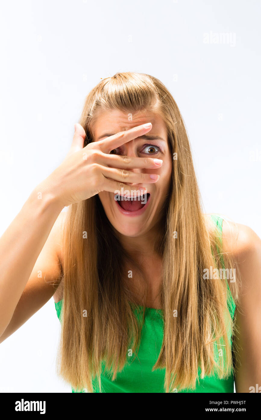 Spaventata donna spiata da dita sopra la faccia Foto Stock