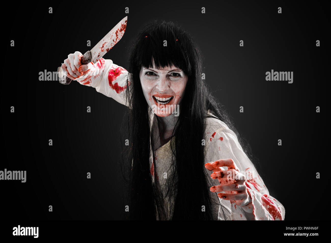 Halloween horror. Crazy sanguinosa scary zombie ragazza con il coltello macellaio cleaver guarda nella fotocamera su sfondo nero Foto Stock