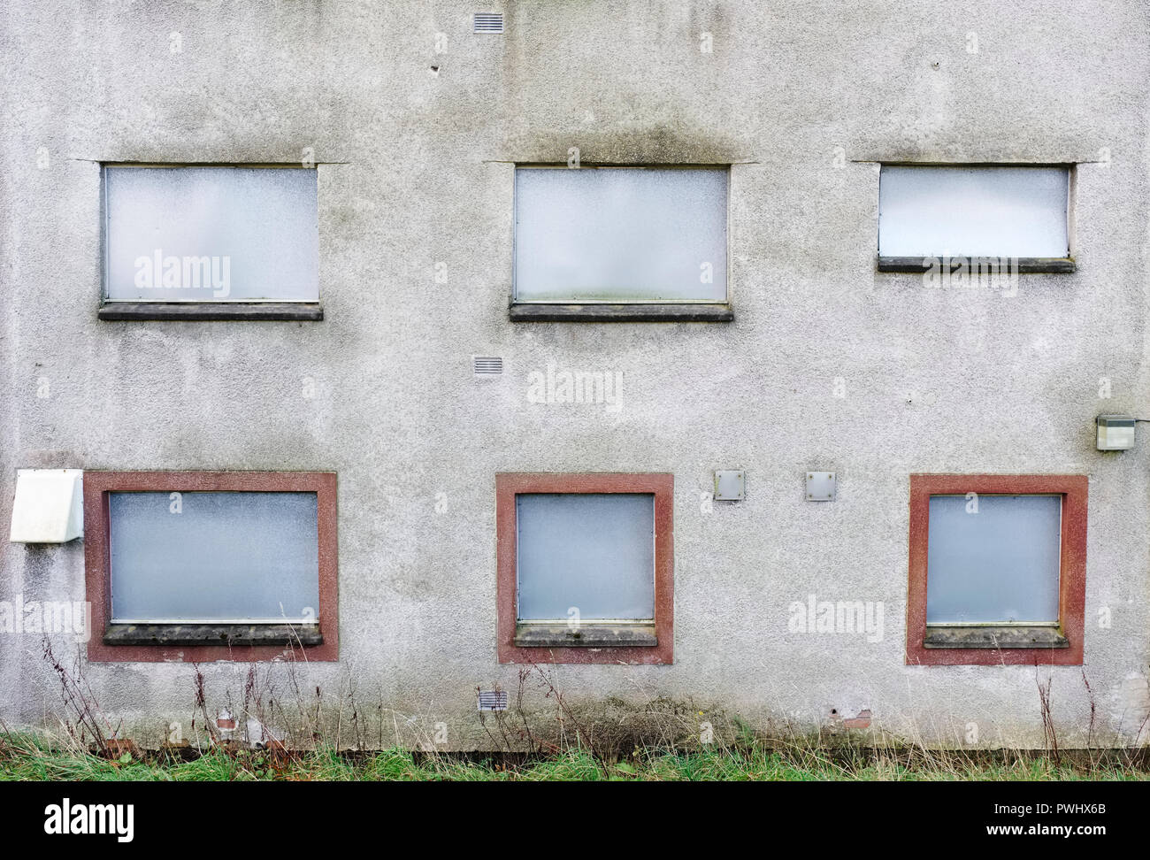 Edificio abbandonato lamiera scheda sopra windows grigio opaco muro sporco Foto Stock
