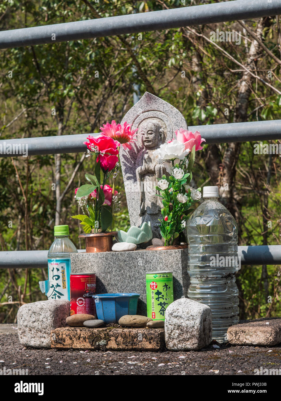 Strada santuario, una statua buddista con fiori di plastica, offerte di ciottoli, bevande, Shimanto, Kochi, Shikoku Giappone Foto Stock