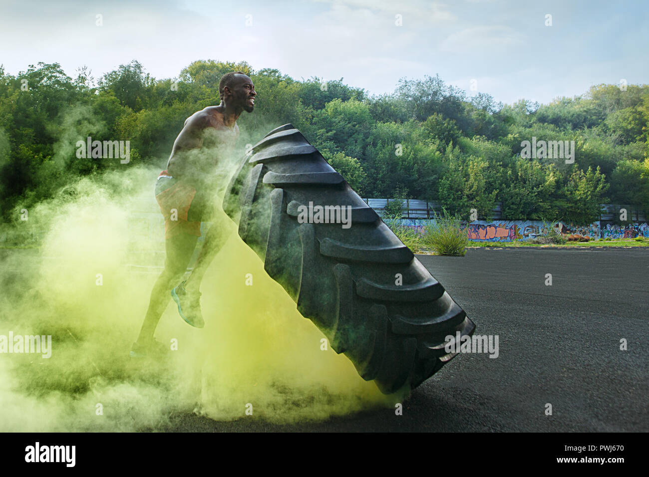 Bello americano africano uomo muscolare flipping bruciando pneumatici grandi outdoor con fumo Foto Stock
