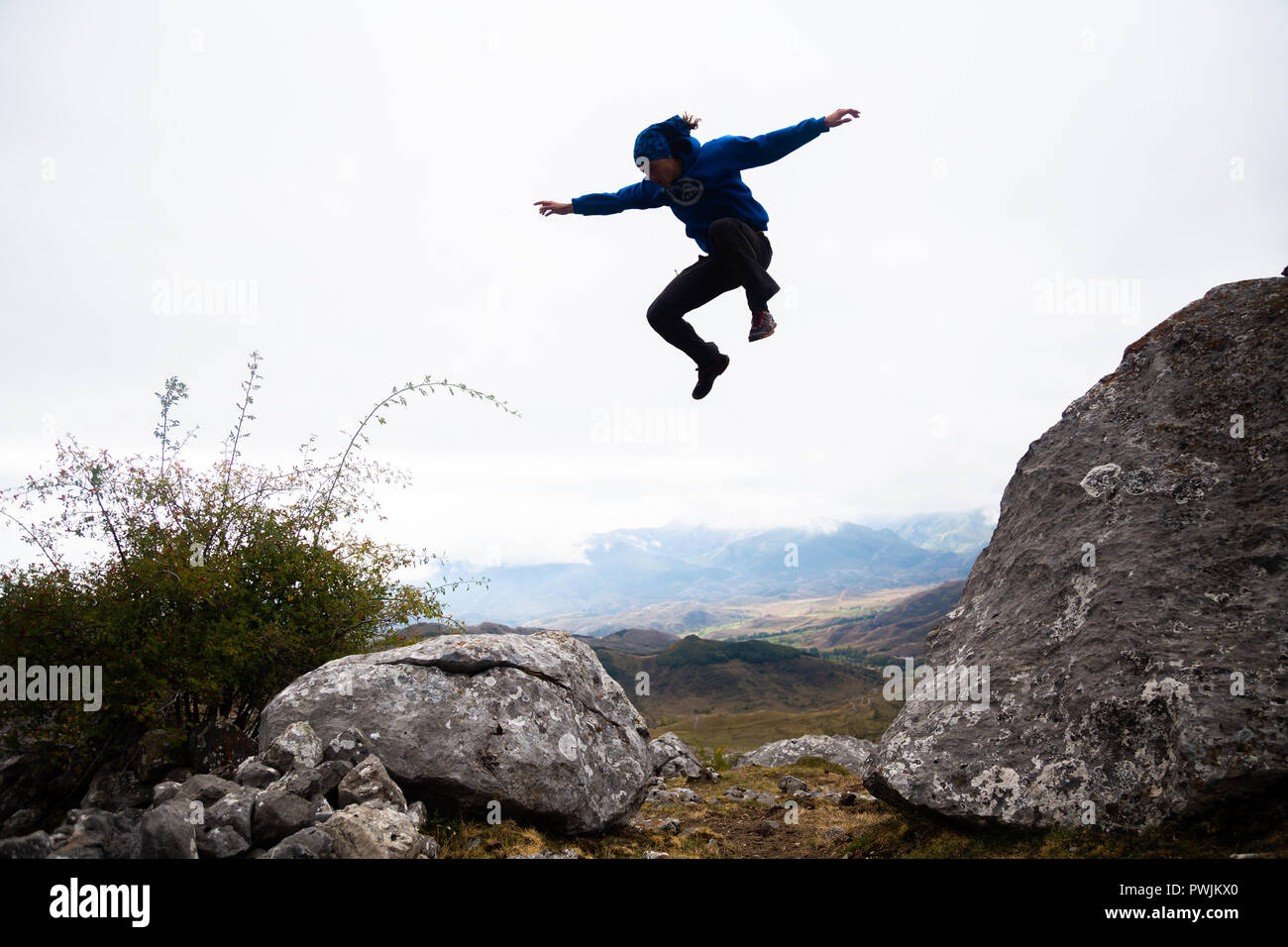 Da sotto vista di uomo sportivo saltando di roccia in roccia facendo parkour nel pomeriggio. Foto Stock